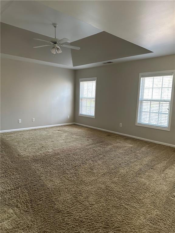 empty room featuring a raised ceiling, carpet flooring, and ceiling fan