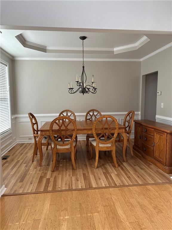 dining area with ornamental molding, light hardwood / wood-style floors, and a raised ceiling