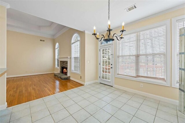 interior space with light tile patterned floors, a tray ceiling, ornamental molding, a stone fireplace, and a chandelier