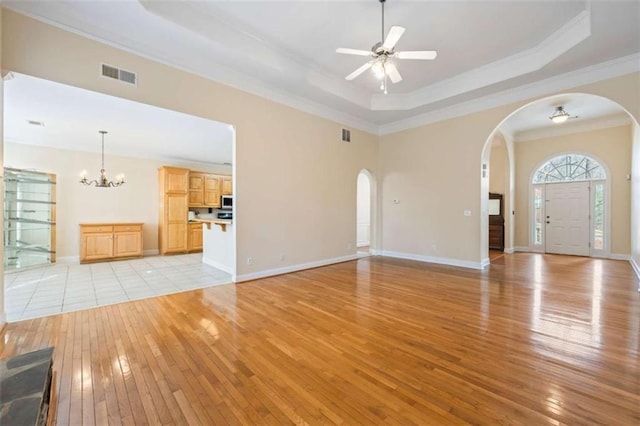 unfurnished living room with crown molding, a raised ceiling, ceiling fan with notable chandelier, and light wood-type flooring