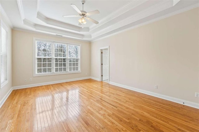 empty room with ceiling fan, ornamental molding, a raised ceiling, and light wood-type flooring