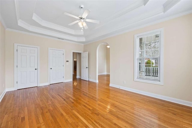 unfurnished bedroom featuring two closets, ornamental molding, ceiling fan, light hardwood / wood-style floors, and a raised ceiling