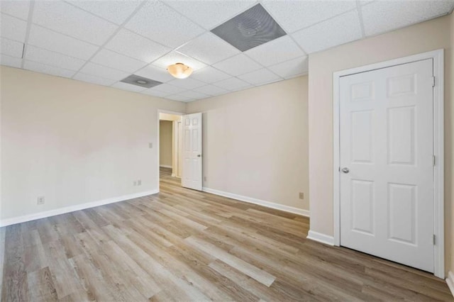 spare room featuring a drop ceiling and light hardwood / wood-style flooring