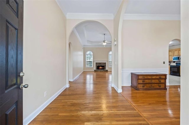 entryway with hardwood / wood-style flooring, ceiling fan, ornamental molding, and a stone fireplace