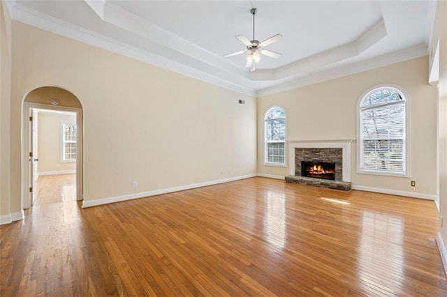 unfurnished living room featuring light wood-type flooring, ornamental molding, a raised ceiling, ceiling fan, and a fireplace