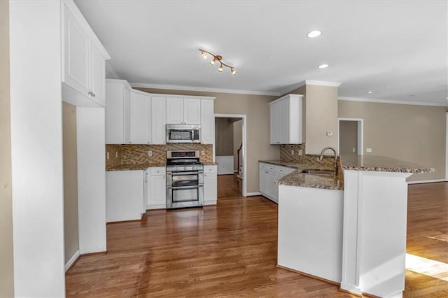 kitchen featuring sink, stainless steel appliances, kitchen peninsula, white cabinets, and dark stone counters