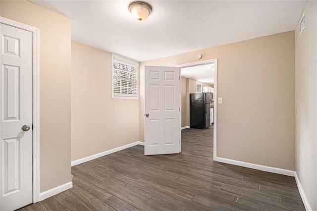 empty room with dark wood-type flooring, visible vents, and baseboards