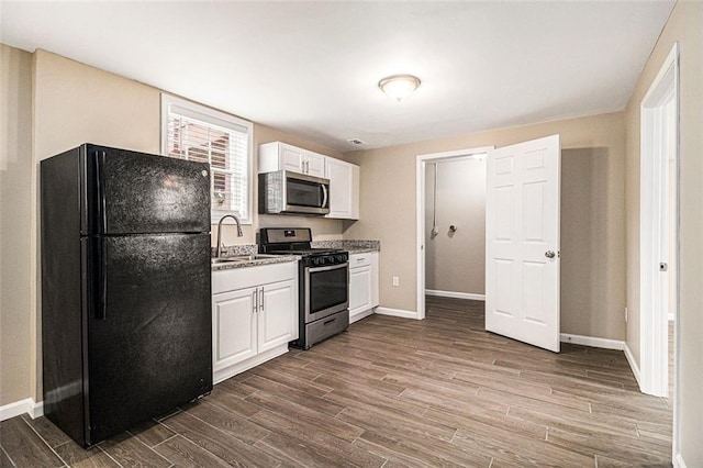 kitchen featuring dark wood-style flooring, a sink, baseboards, white cabinets, and appliances with stainless steel finishes