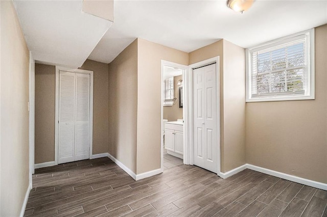 unfurnished bedroom with dark wood-style floors, baseboards, and ensuite bathroom