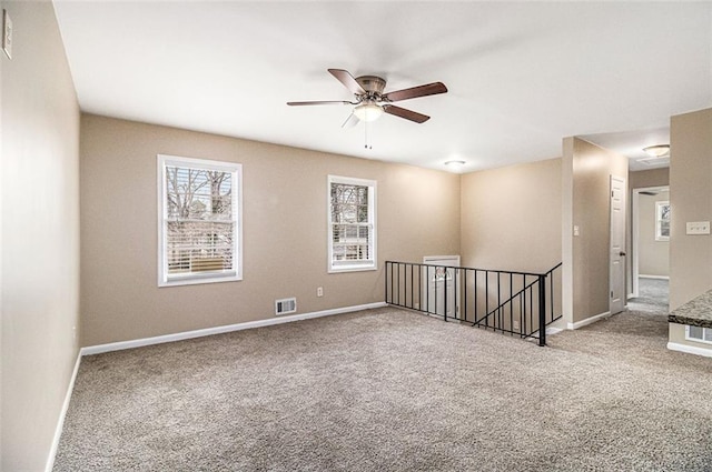 carpeted empty room featuring baseboards, visible vents, and a ceiling fan