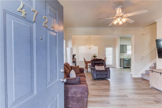 entryway featuring baseboards, stairway, ornamental molding, light wood-type flooring, and ceiling fan with notable chandelier