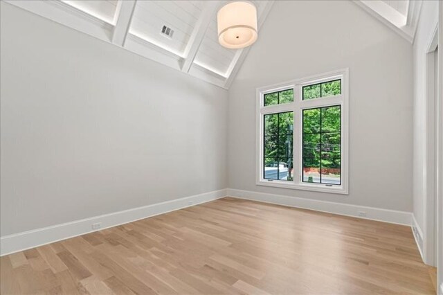 empty room featuring light hardwood / wood-style flooring, beam ceiling, and high vaulted ceiling