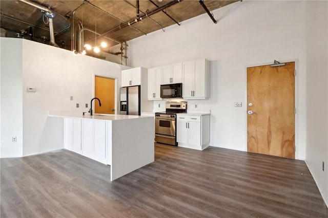 kitchen with appliances with stainless steel finishes, a towering ceiling, white cabinetry, sink, and dark wood-type flooring