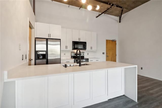 kitchen with dark wood-type flooring, appliances with stainless steel finishes, kitchen peninsula, a towering ceiling, and white cabinets