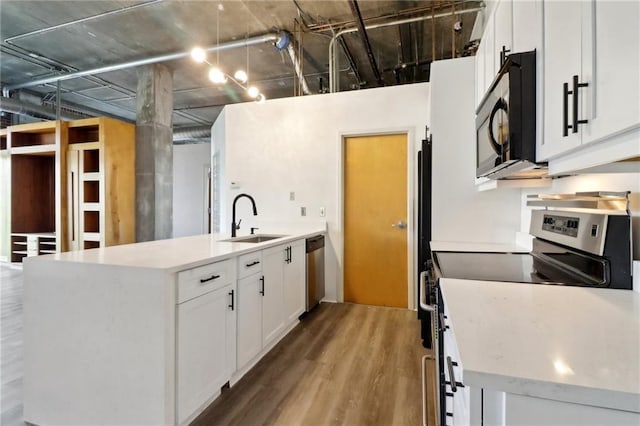 kitchen with appliances with stainless steel finishes, an island with sink, sink, white cabinets, and hardwood / wood-style flooring