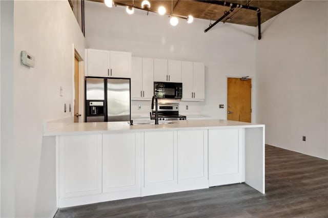 kitchen with white cabinets, a high ceiling, kitchen peninsula, stainless steel appliances, and dark wood-type flooring