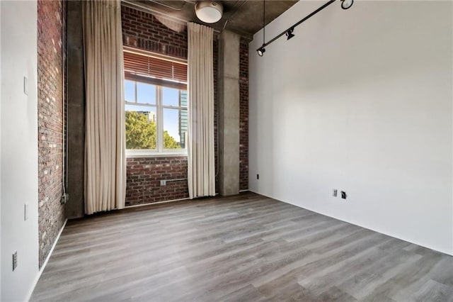 spare room featuring wood-type flooring, brick wall, and track lighting