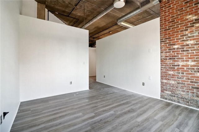 spare room featuring dark wood-type flooring and brick wall