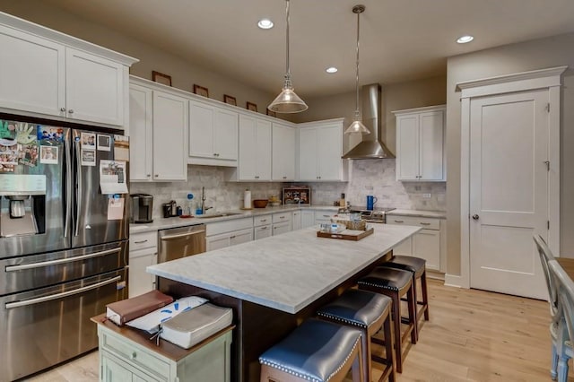 kitchen featuring a center island, wall chimney range hood, white cabinetry, and stainless steel appliances