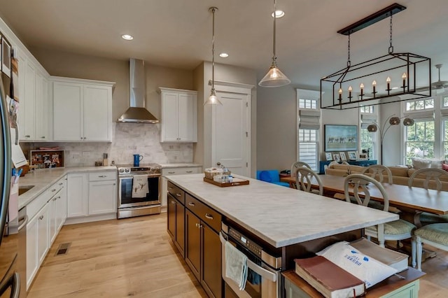 kitchen featuring decorative light fixtures, a center island, stainless steel electric range oven, wall chimney exhaust hood, and white cabinetry