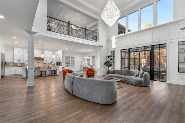 living room with dark wood-type flooring, a high ceiling, an inviting chandelier, and decorative columns