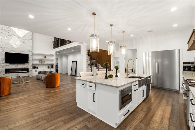 kitchen featuring white cabinetry, dark hardwood / wood-style flooring, a premium fireplace, an island with sink, and light stone countertops