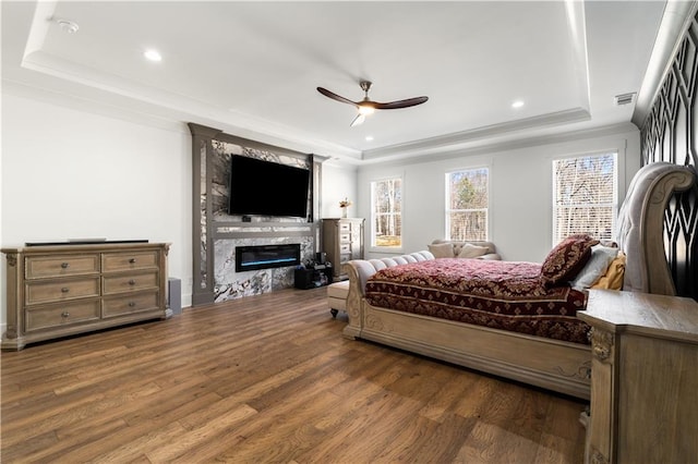 bedroom featuring a fireplace, dark hardwood / wood-style flooring, a tray ceiling, and ceiling fan