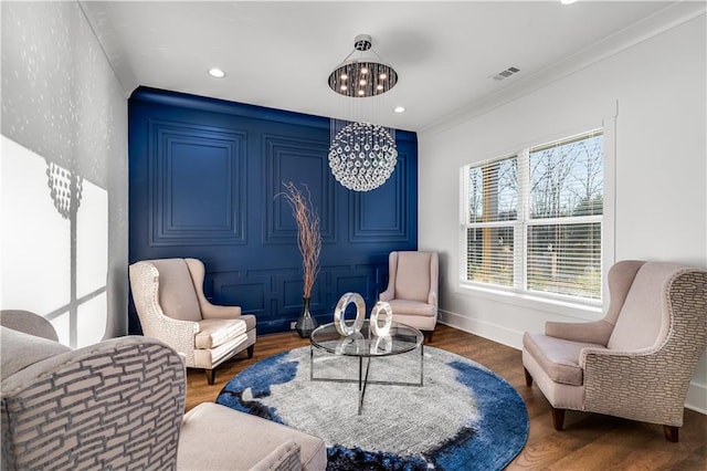 sitting room with ornamental molding, a notable chandelier, and wood-type flooring