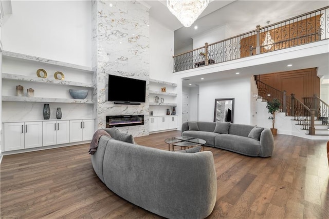 living room featuring built in features, wood-type flooring, a high end fireplace, and a towering ceiling