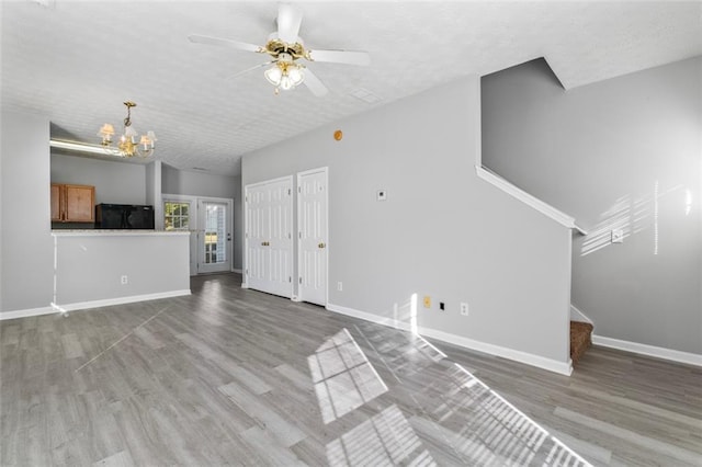 unfurnished living room featuring hardwood / wood-style floors, a textured ceiling, and ceiling fan with notable chandelier