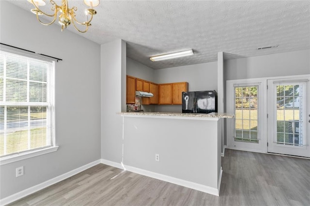 kitchen with kitchen peninsula, a textured ceiling, light wood-type flooring, and black refrigerator