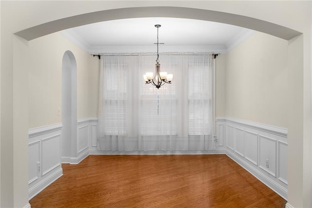 unfurnished dining area with wood-type flooring, crown molding, and a chandelier