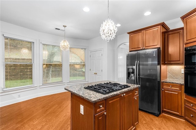 kitchen with an inviting chandelier, light wood-type flooring, hanging light fixtures, black appliances, and a center island