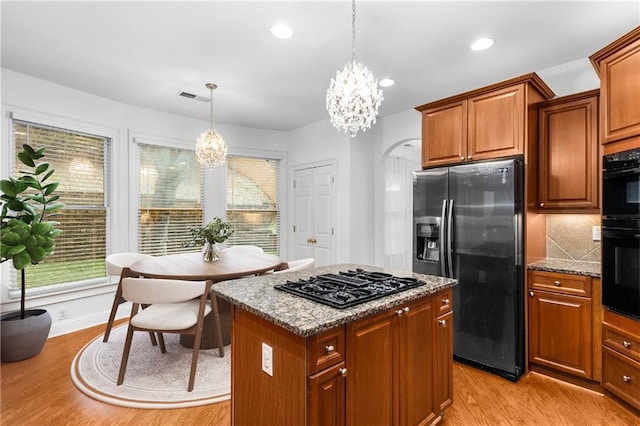 kitchen featuring a notable chandelier, pendant lighting, black appliances, light hardwood / wood-style flooring, and light stone countertops