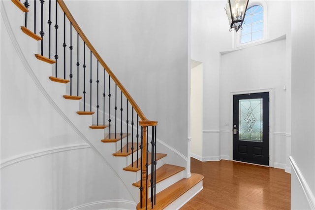 entryway with a towering ceiling, wood-type flooring, and a notable chandelier