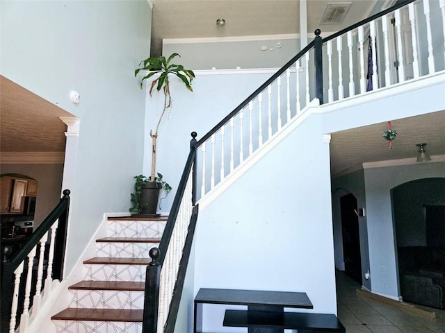 stairway with crown molding, tile patterned floors, and a high ceiling