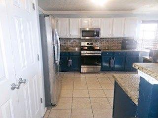 kitchen with light tile patterned floors, appliances with stainless steel finishes, white cabinets, blue cabinets, and decorative backsplash