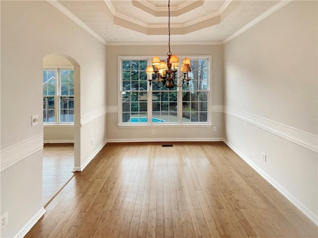 unfurnished dining area featuring ornamental molding, arched walkways, wood-type flooring, a raised ceiling, and a chandelier