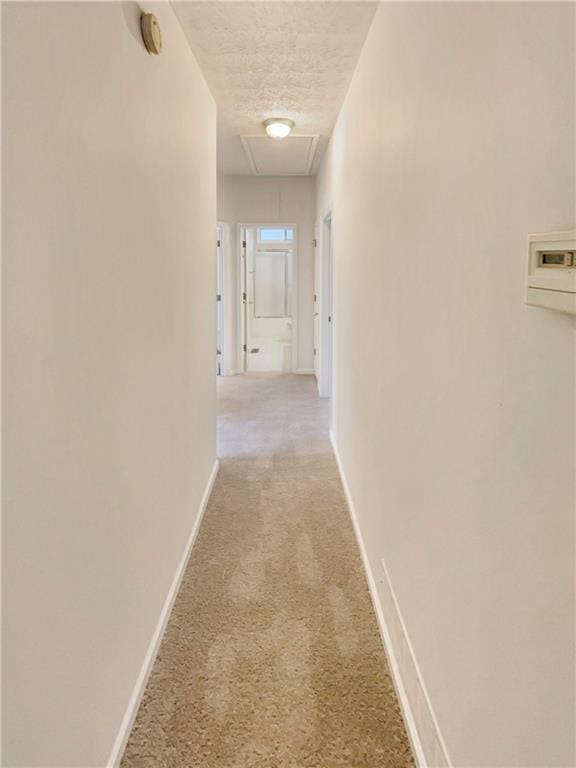 hallway featuring baseboards, light carpet, and a textured ceiling