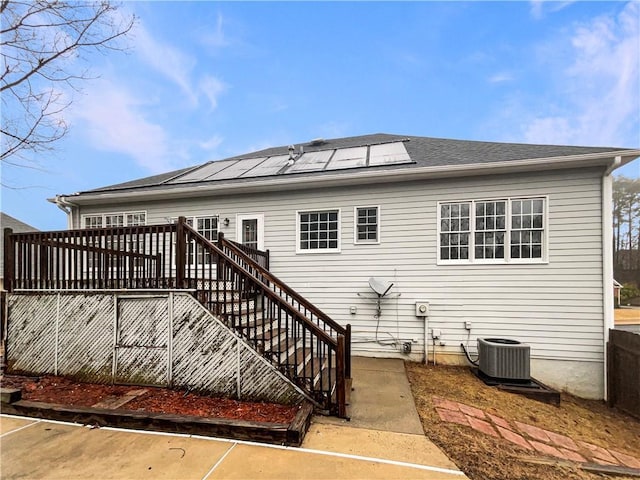 rear view of house featuring a shingled roof, stairs, central AC, roof mounted solar panels, and a deck