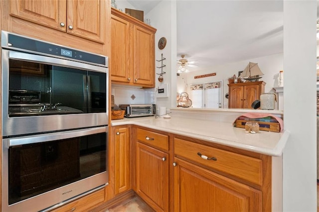 kitchen with tasteful backsplash, double oven, kitchen peninsula, and ceiling fan