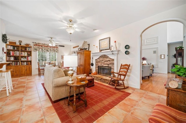 living room featuring ceiling fan, light tile patterned floors, and a stone fireplace