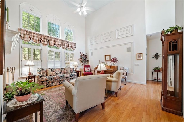 living room with light wood-type flooring, ceiling fan, a wealth of natural light, and a high ceiling