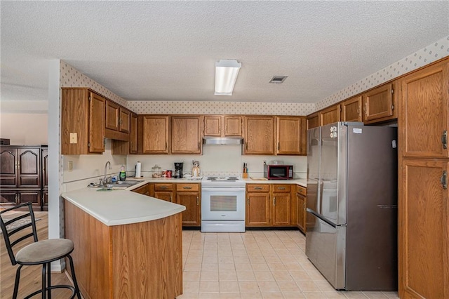 3264 Salem Cove Trl SE, Conyers, GA 30013 - kitchen with freestanding refrigerator, electric range, brown cabinetry, a peninsula, and a textured ceiling