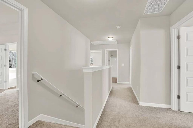 hallway featuring baseboards, visible vents, light carpet, and an upstairs landing