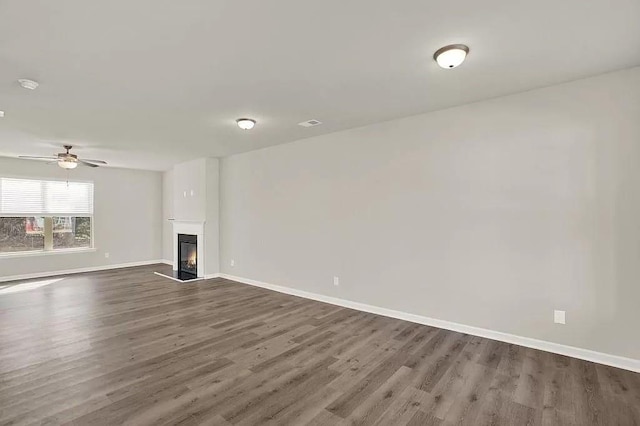 unfurnished living room featuring a glass covered fireplace, dark wood-type flooring, baseboards, and ceiling fan