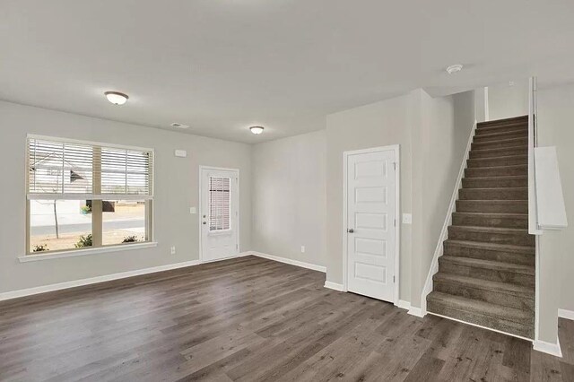 unfurnished living room featuring stairs, wood finished floors, and baseboards