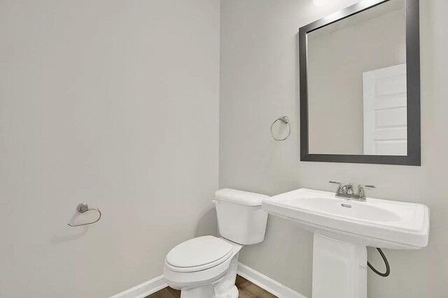 half bath featuring baseboards and toilet