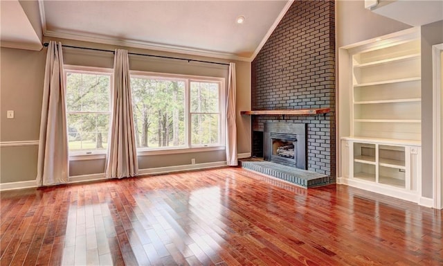 unfurnished living room featuring built in shelves, lofted ceiling, ornamental molding, a fireplace, and hardwood / wood-style floors