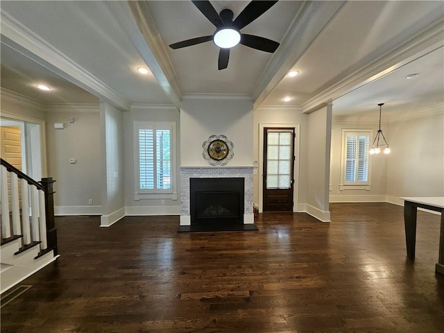 unfurnished living room with ceiling fan with notable chandelier, dark hardwood / wood-style flooring, ornamental molding, and a tiled fireplace